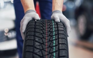 Nahaufnahme eines neuen Autoreifens, der von einer Person gehalten wird.