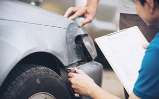 Begutachtung eines Unfallschadens an der Fahrzeugfront mit Klemmbrett und Dokumentation.